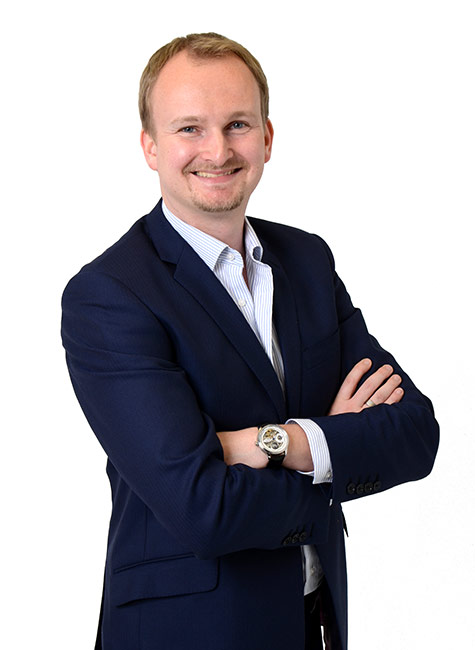 Portrait photo of a businessman wearing a suit and a watch smiling at the camera, against a white background.