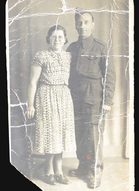 Old, damaged photo of a soldier standing next to a woman.