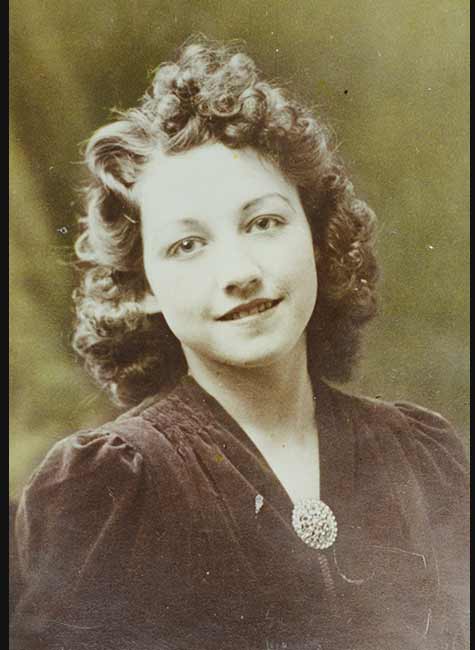 An old colour photograph of a woman smiling at the camera. The photo is faded and there are flecks of noise.